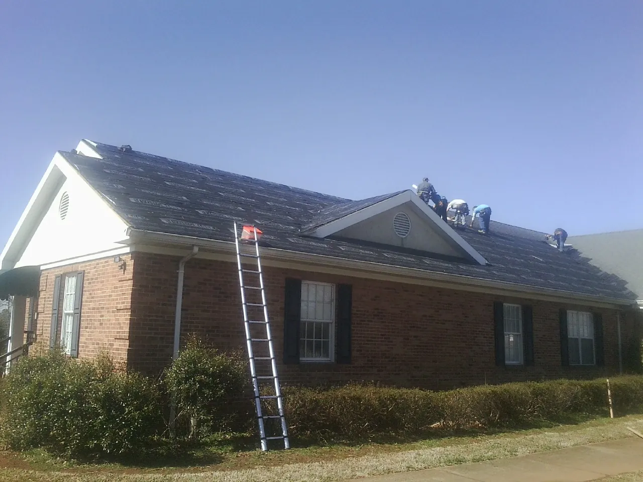 Crew tearing shingles off a brick ranch roof with a ladder set — Emergency Roof Repair work by our crew in Shipman
