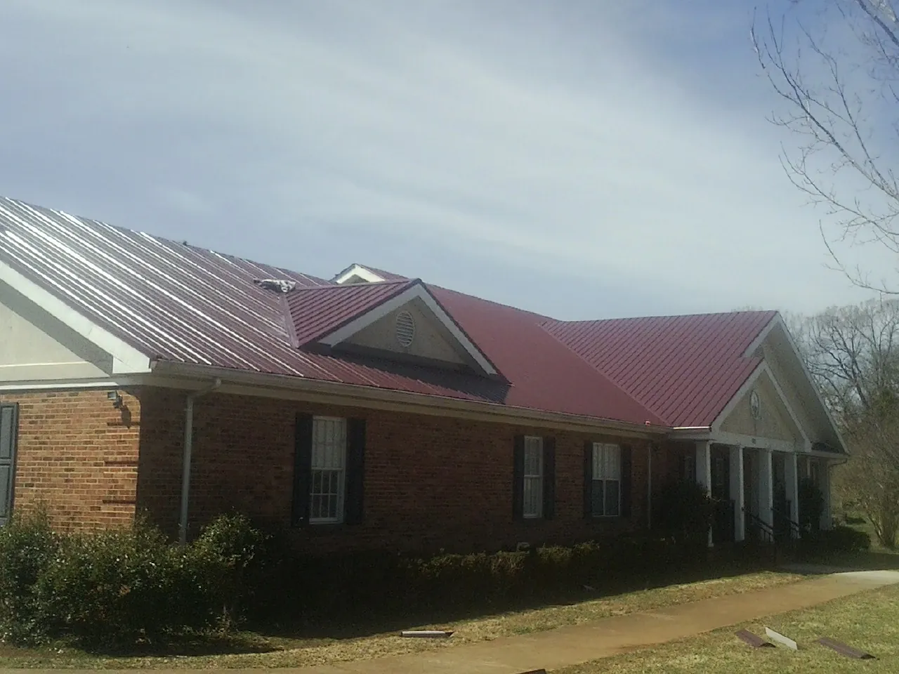 Red metal roof with gabled entries on a long brick building, from a Hail Damage Roof Repair job in Shipman