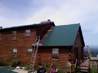 Green metal roof going on a two story log home with ladders set in Shipman