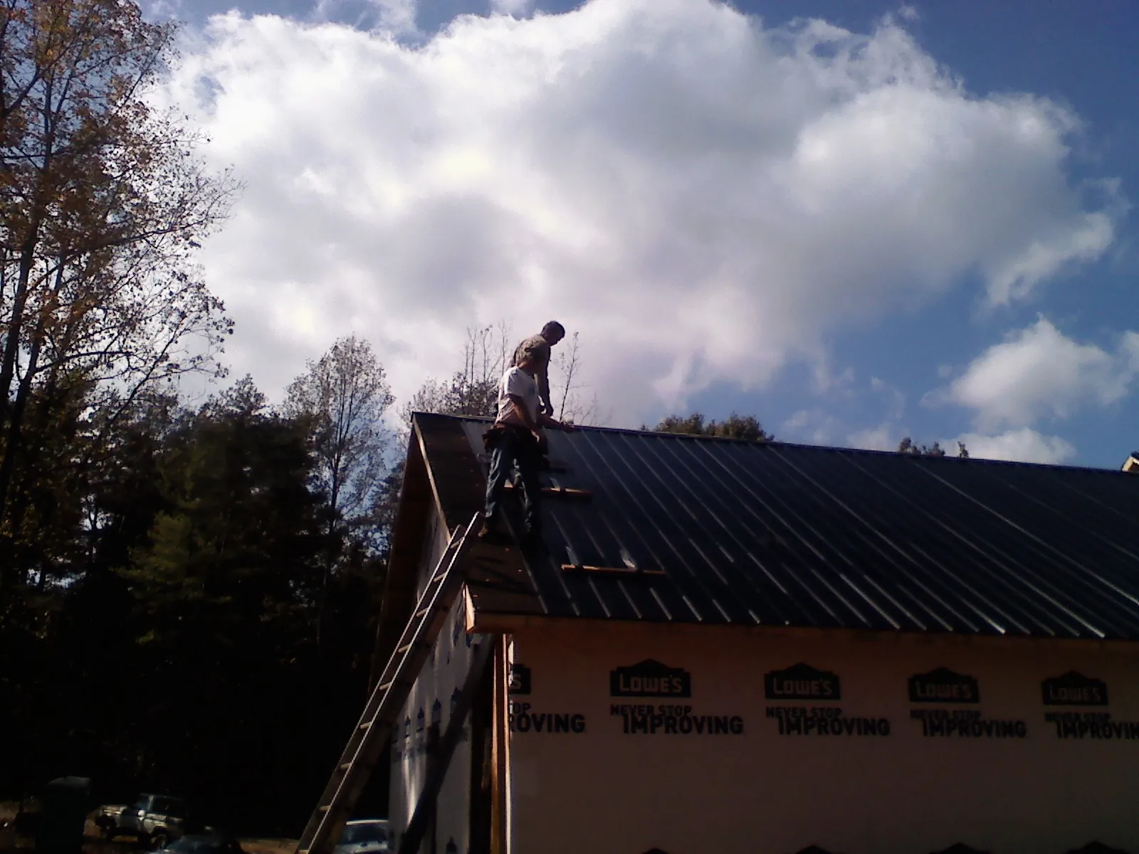 Roofer fastening dark metal panels high against a cloudy sky, from a Roof Inspection job in Shipman