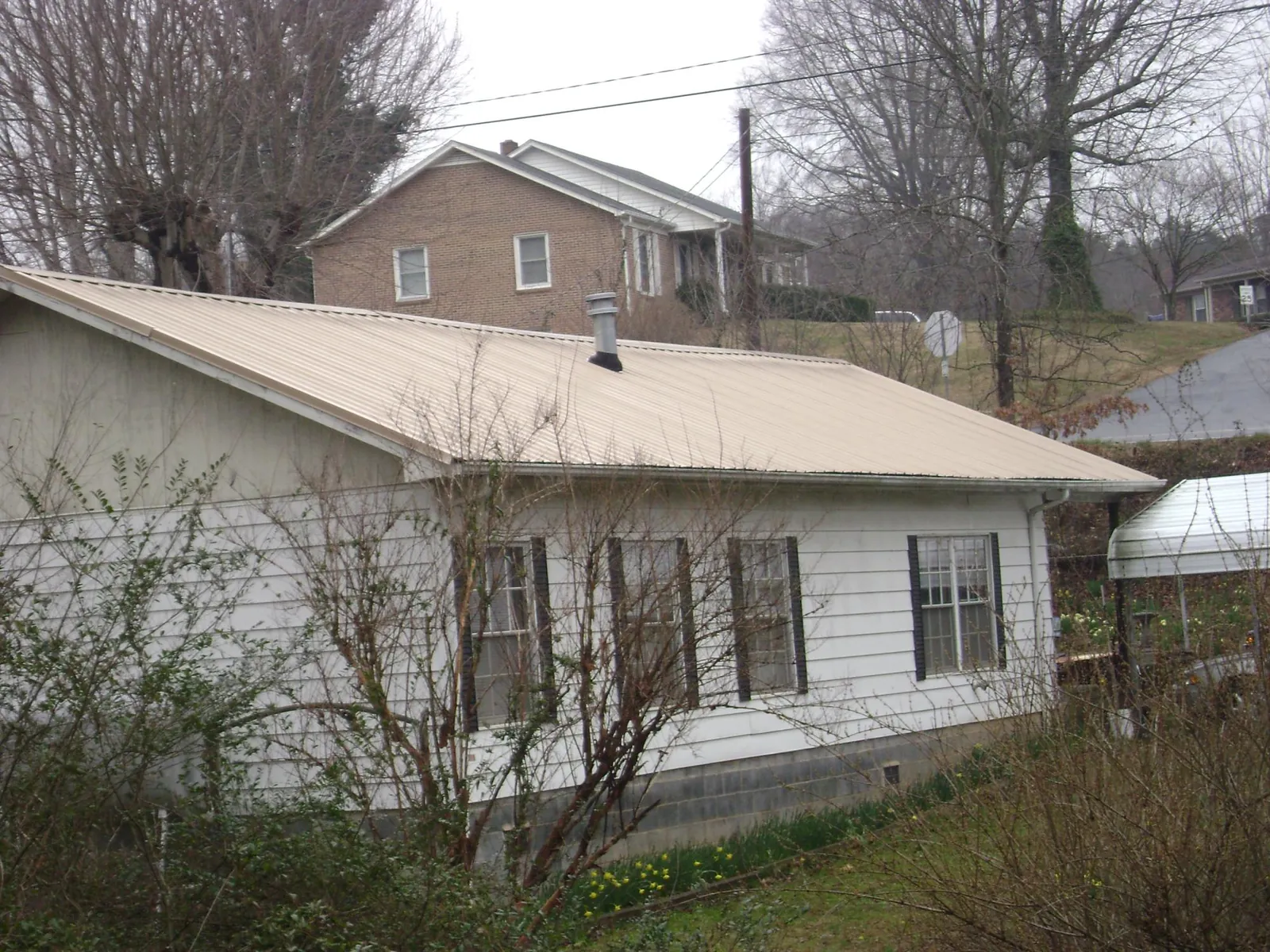 Tan metal roof on a white sided house set into a hillside — Commercial Roofing by Roofing Brothers in Shipman